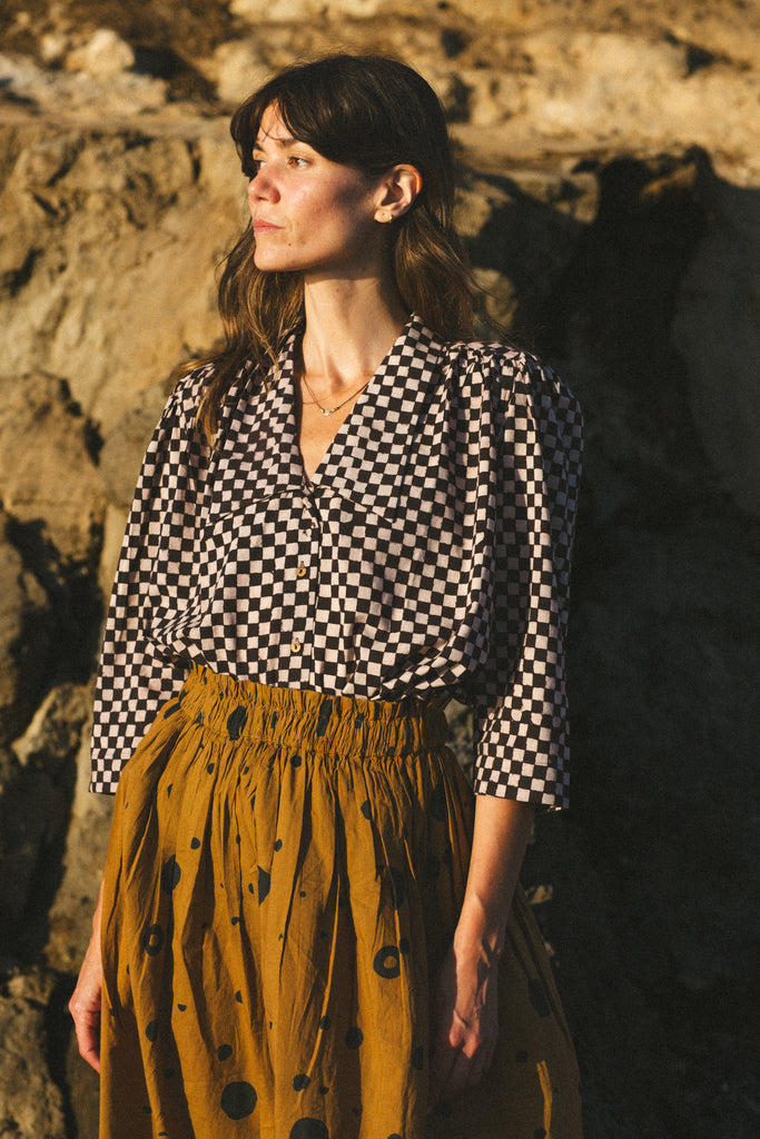 A black and white checkered blouse with a Victorian collar paired with a yellow skirt, showcasing vintage elegance.