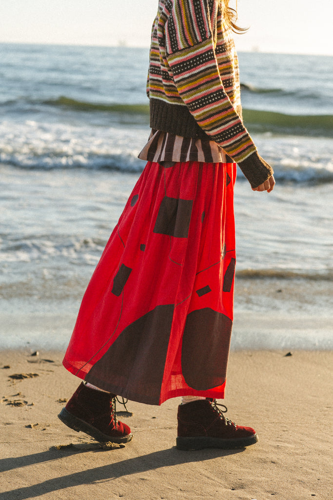 A bold red skirt with brown accents, showcasing unique appliqué craftsmanship and a versatile mid-calf length.