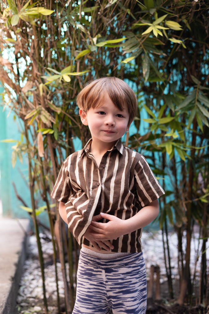 A short-sleeved, brown-and-white striped button-up shirt with a structured collar. The shirt has a relaxed fit and a slightly cropped length, giving it a casual and comfortable look. Made from lightweight fabric, it pairs seamlessly with matching striped shorts for a coordinated outfit.