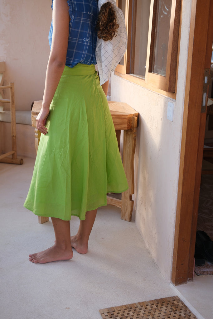 Discover effortless elegance with our hand-woven cotton wrap skirt, showcased in a vibrant parrot green. A woman models this summer-ready piece, paired with a chic hat, illustrating its ideal blend of style and sustainability. Crafted with care for environmentally-conscious fashion lovers, this midi-length skirt is perfect for embracing the sunny season in sustainable sophistication