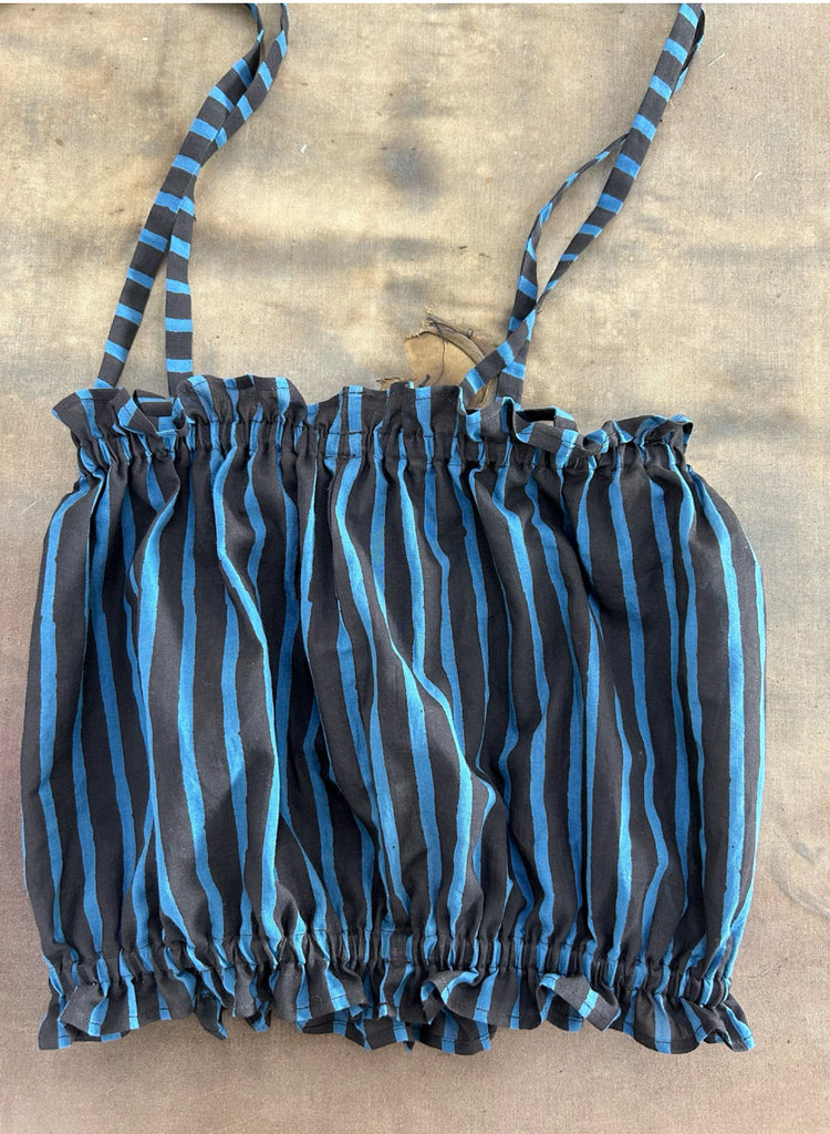 A sleeveless children's top with a ruched, gathered design and thin shoulder straps, featuring a black base with bright blue vertical stripes. The fabric has a lightweight, airy appearance, and the hem and neckline are elasticated for a snug fit. 