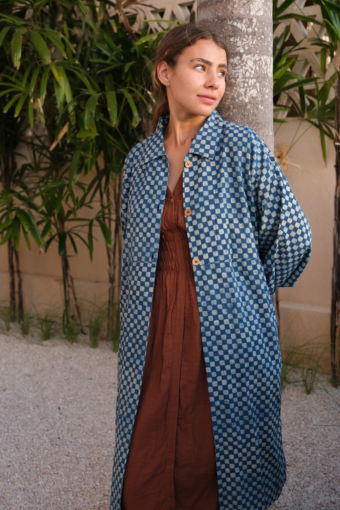 Introducing our Indigo Checkered Duster Jacket, a versatile wardrobe staple made from handwoven cotton. Featuring a classic indigo and white checkered block print, this jacket combines style and comfort effortlessly. With a straight collar, coconut buttons, and a relaxed fit, it’s perfect for layering over both dressy and casual outfits.