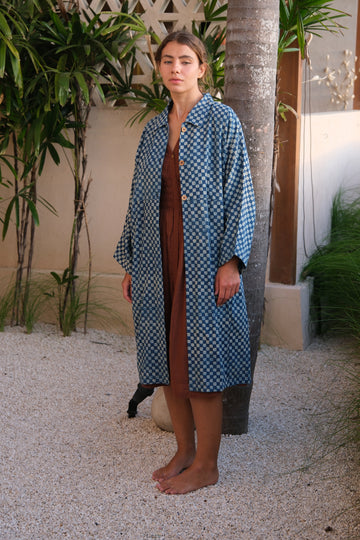 Introducing our Indigo Checkered Duster Jacket, a versatile wardrobe staple made from handwoven cotton. Featuring a classic indigo and white checkered block print, this jacket combines style and comfort effortlessly. With a straight collar, coconut buttons, and a relaxed fit, it’s perfect for layering over both dressy and casual outfits.