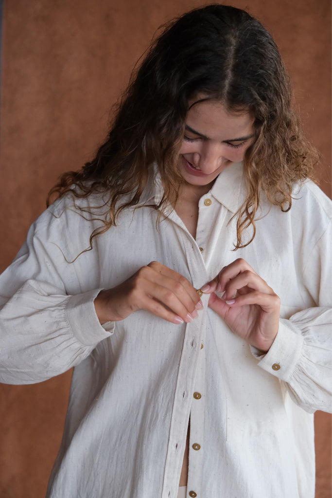 Introducing the White Artist Smock, a collaboration between Audrey E Leary and World of Crow. This short-length smock, crafted from thick, handwoven organic cotton, features a straight collar, puff full sleeves, and gathered cuffs. With spacious pockets and a comfortable fit, it's ideal for painting, crafting, and staying cozy during travel.