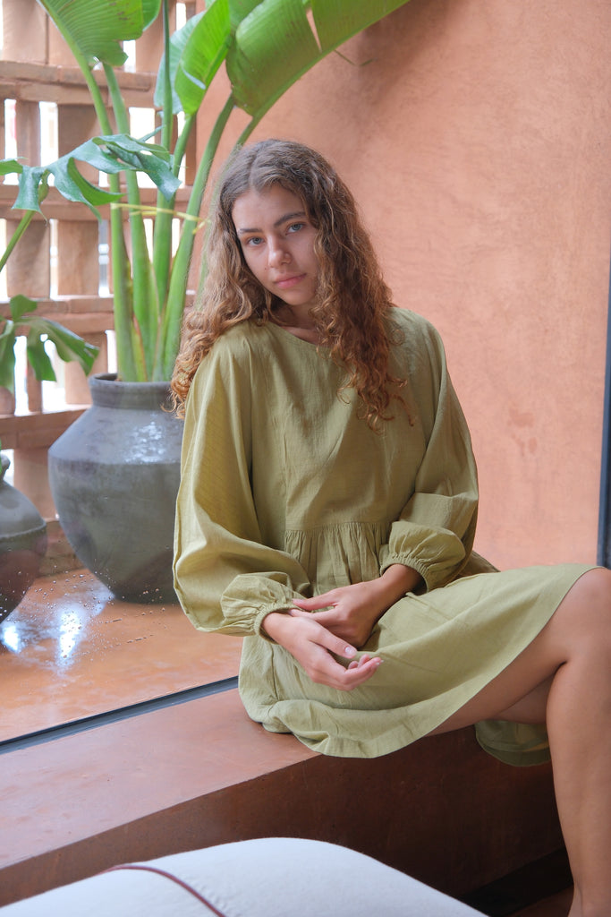 Introducing the Olive Get Away Dress, a collaboration between Audrey E Leary and World of Crow. This mini dress in unique olive green features a scoop neck and three-quarter puff sleeves, crafted from soft, handwoven cotton. Sustainably made and breathable, it offers a comfortable, true-to-size fit with lightweight, non-stretchy fabric, ideal for everyday wear.