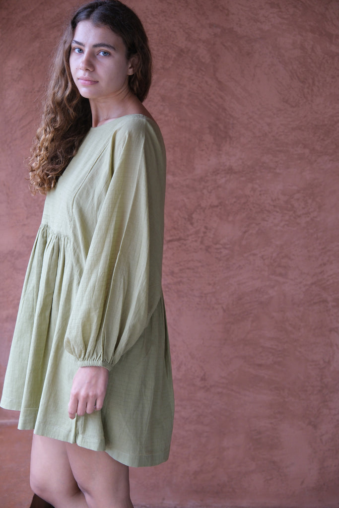 Introducing the Olive Get Away Dress, a collaboration between Audrey E Leary and World of Crow. This mini dress in unique olive green features a scoop neck and three-quarter puff sleeves, crafted from soft, handwoven cotton. Sustainably made and breathable, it offers a comfortable, true-to-size fit with lightweight, non-stretchy fabric, ideal for everyday wear.