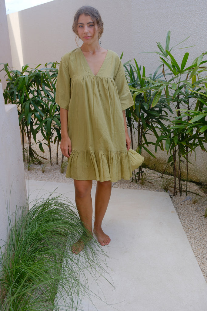 Introducing our Olive Green Day Dress by Audrey E Leary and World of Crow. This mini-length dress features a V-neck, drop shoulders, and a unique olive green color. Made from soft, handwoven cotton, it offers a comfortable, lightweight fit perfect for everyday wear