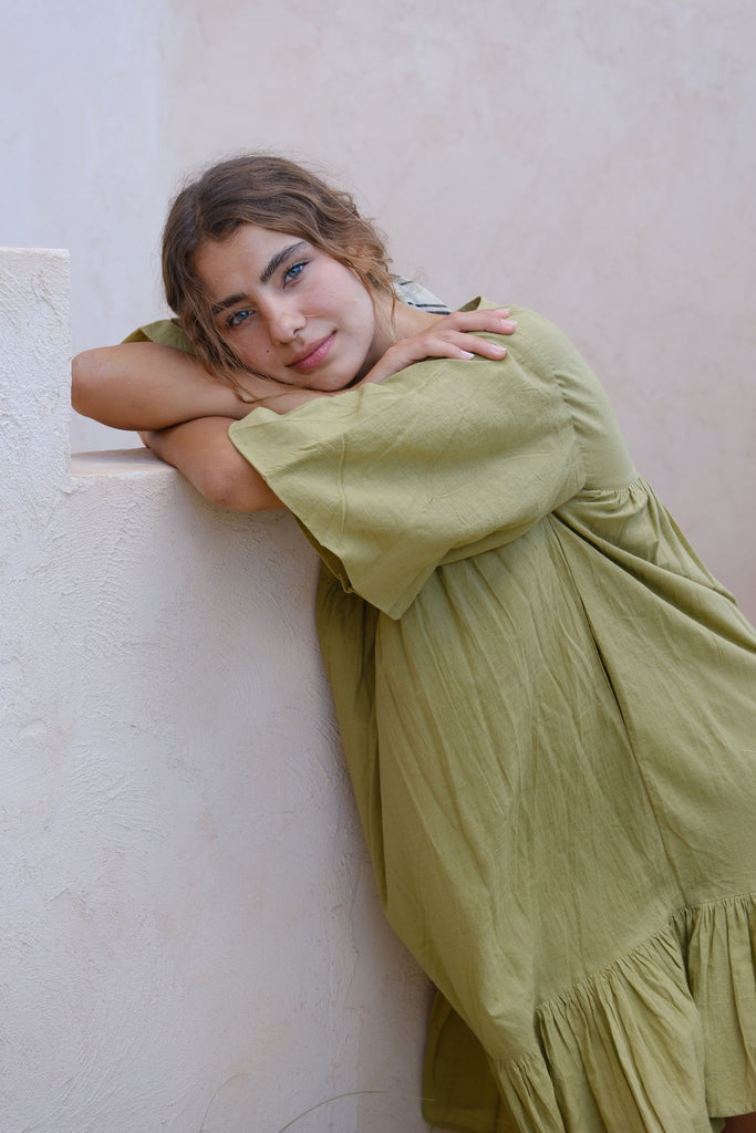 Introducing our Olive Green Day Dress by Audrey E Leary and World of Crow. This mini-length dress features a V-neck, drop shoulders, and a unique olive green color. Made from soft, handwoven cotton, it offers a comfortable, lightweight fit perfect for everyday wear