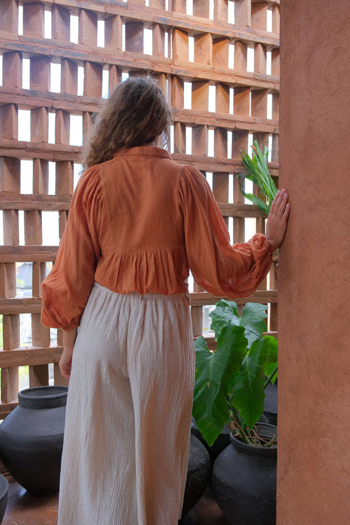 Introducing the Audrey X Crow Collection, featuring a woman in an orange Jane Austen Shirt and white skirt. This collection showcases hand-woven fabric with block-printed stripes, embodying elegance and artisanal craftsmanship. The vibrant orange and classic white combination adds a touch of sophistication to this beautifully crafted ensemble.