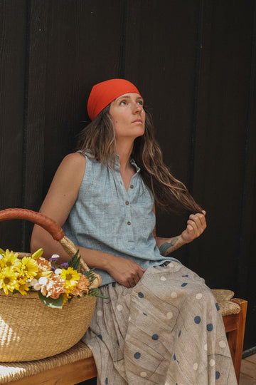 Sleeveless chambray blue top made from soft, handwoven organic cotton. Features a short button placket at the front and a subtle pleat detail below the collar, creating a clean and structured look. The stand collar adds a modern touch, while the breathable, lightweight fabric ensures comfort in warmer weather. Naturally dyed and ethically crafted, this top is perfect for effortless, everyday wear.