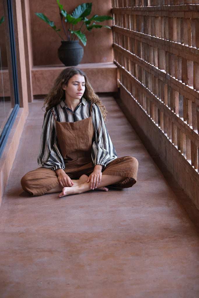 Introducing the Jane Austen Shirt from the Audrey X Crow Collection, elegantly worn by a woman in overalls. Seated on the floor, she effortlessly showcases the shirt's timeless design and refined craftsmanship