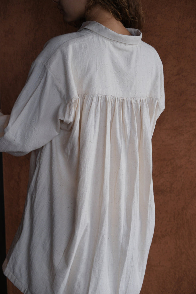 Introducing the White Artist Smock, a collaboration between Audrey E Leary and World of Crow. This short-length smock, crafted from thick, handwoven organic cotton, features a straight collar, puff full sleeves, and gathered cuffs. With spacious pockets and a comfortable fit, it's ideal for painting, crafting, and staying cozy during travel.