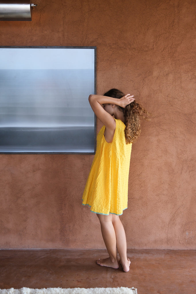 Introducing the Yellow Crinkly Dress, a collaboration between Audrey E Leary and World of Crow. This vibrant yellow mini dress features a sleeveless design and is crafted from handwoven cotton with a crinkly texture. Sustainably made, it combines minimalist style with comfort for a chic and eco-friendly wardrobe staple