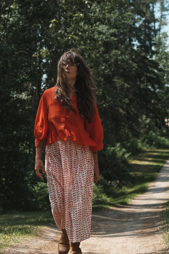 A lightweight, mid-length skirt by World of Crow featuring a soft, flowing texture that moves gracefully with the breeze. The skirt is crafted in a gentle off-white base adorned with hand-printed rust-red geometric motifs, creating a subtle yet striking pattern. Designed with a relaxed silhouette and gathered waist, it exudes an effortless, breezy charm perfect for warm, sunlit days. The fabric is  airy and breathable, offering comfort and elegance in equal measure.