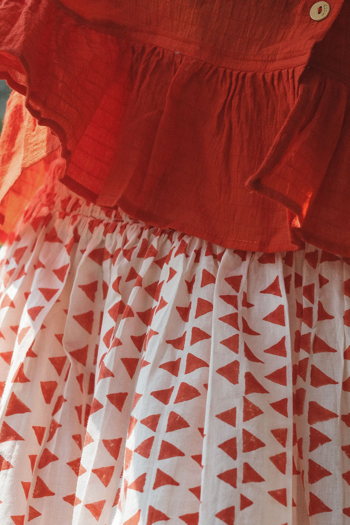A lightweight, mid-length skirt by World of Crow featuring a soft, flowing texture that moves gracefully with the breeze. The skirt is crafted in a gentle off-white base adorned with hand-printed rust-red geometric motifs, creating a subtle yet striking pattern. Designed with a relaxed silhouette and gathered waist, it exudes an effortless, breezy charm perfect for warm, sunlit days. The fabric is  airy and breathable, offering comfort and elegance in equal measure.