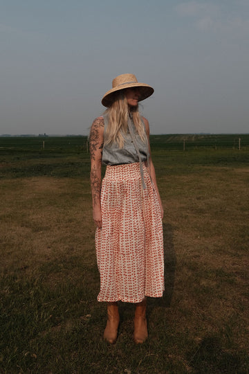 A lightweight, mid-length skirt by World of Crow featuring a soft, flowing texture that moves gracefully with the breeze. The skirt is crafted in a gentle off-white base adorned with hand-printed rust-red geometric motifs, creating a subtle yet striking pattern. Designed with a relaxed silhouette and gathered waist, it exudes an effortless, breezy charm perfect for warm, sunlit days. The fabric is  airy and breathable, offering comfort and elegance in equal measure.