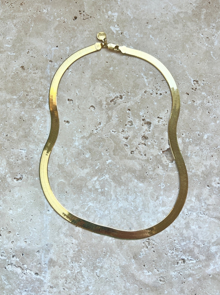 Introducing our gold herringbone necklace, a vintage-inspired statement piece made in Italy. This necklace features a striking 18" length and 7mm thickness, elegantly plated in 14k yellow gold. Its classic design and luxurious finish make it a timeless addition to any jewelry collection.